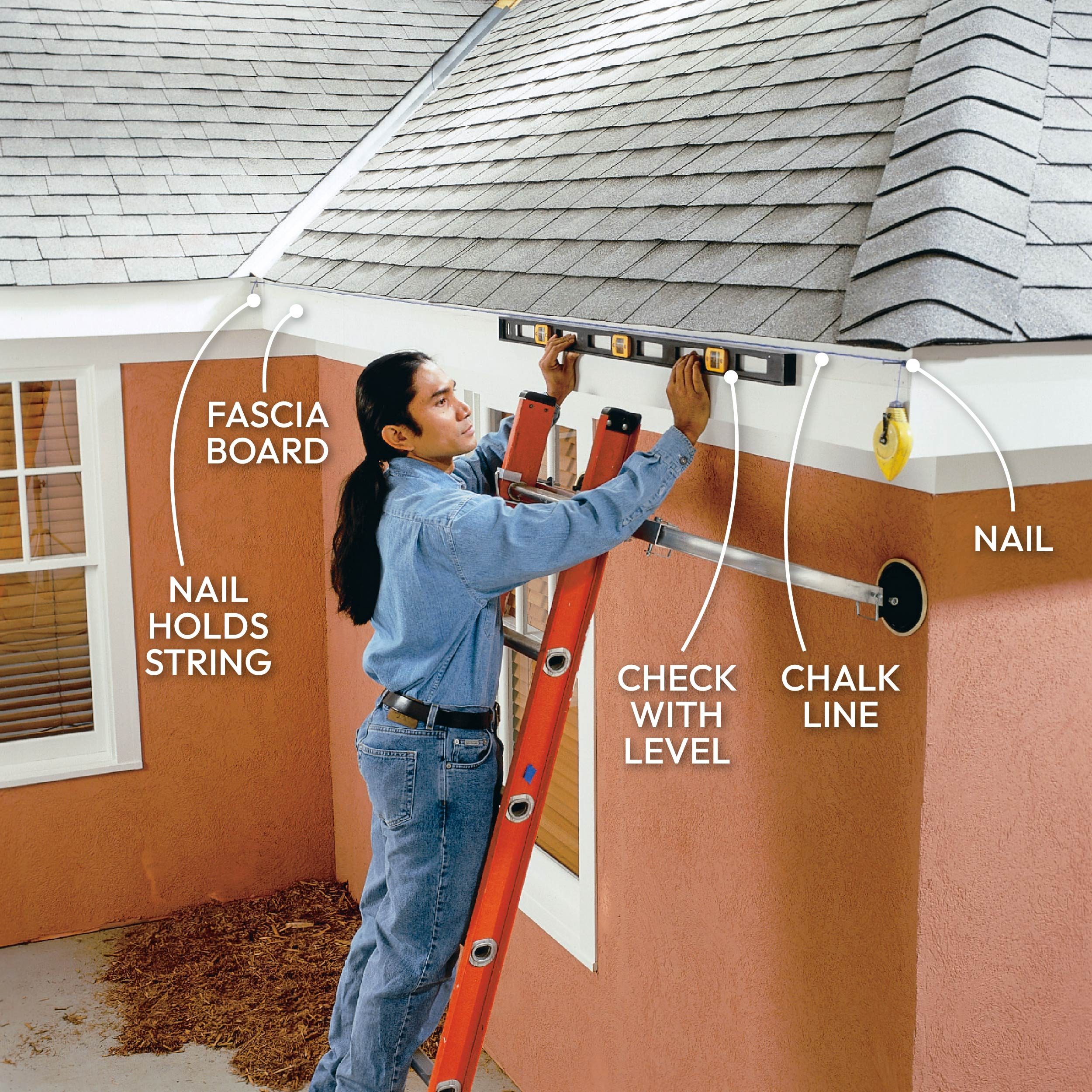 A person uses a level to align a fascia board while standing on a ladder near a sloped roof, with tools and a chalk line visible.