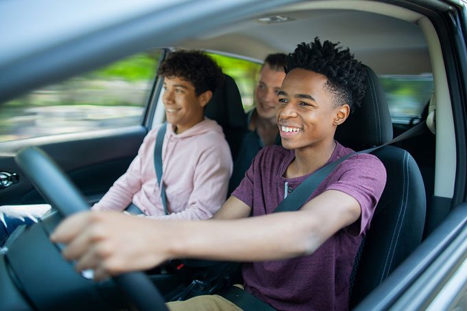 Young Black ethnicity teenager boy driving car while Multiracial Hispanic Caucasian friend sits in car with friend passenger