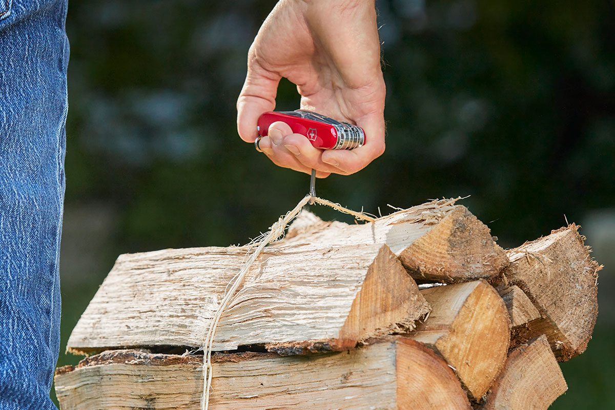 A person holding a bunch of wood with a swiss army knife