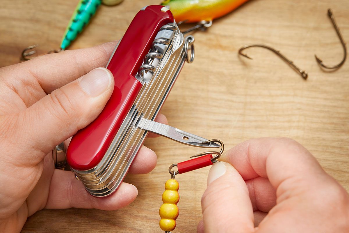 Closeup of a hand sharpening the fishing hook with a swiss army knife