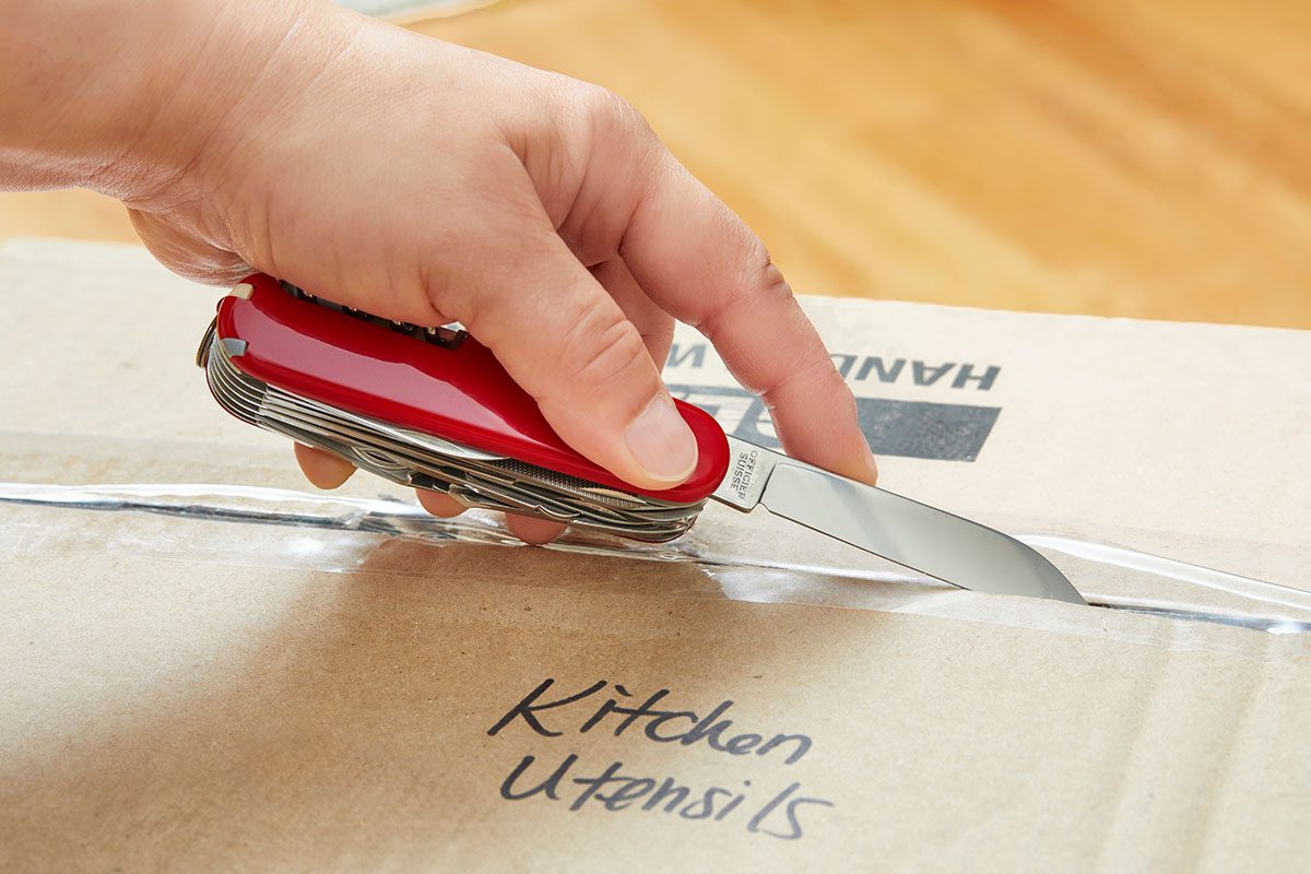 A closeup of a hand cutting a box with swiss army knife
