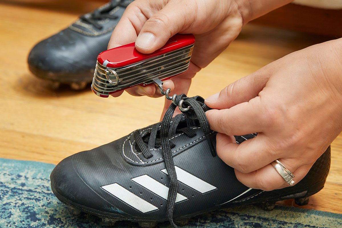 A closeup of a hand fixing the shoe laces with swiss army knife