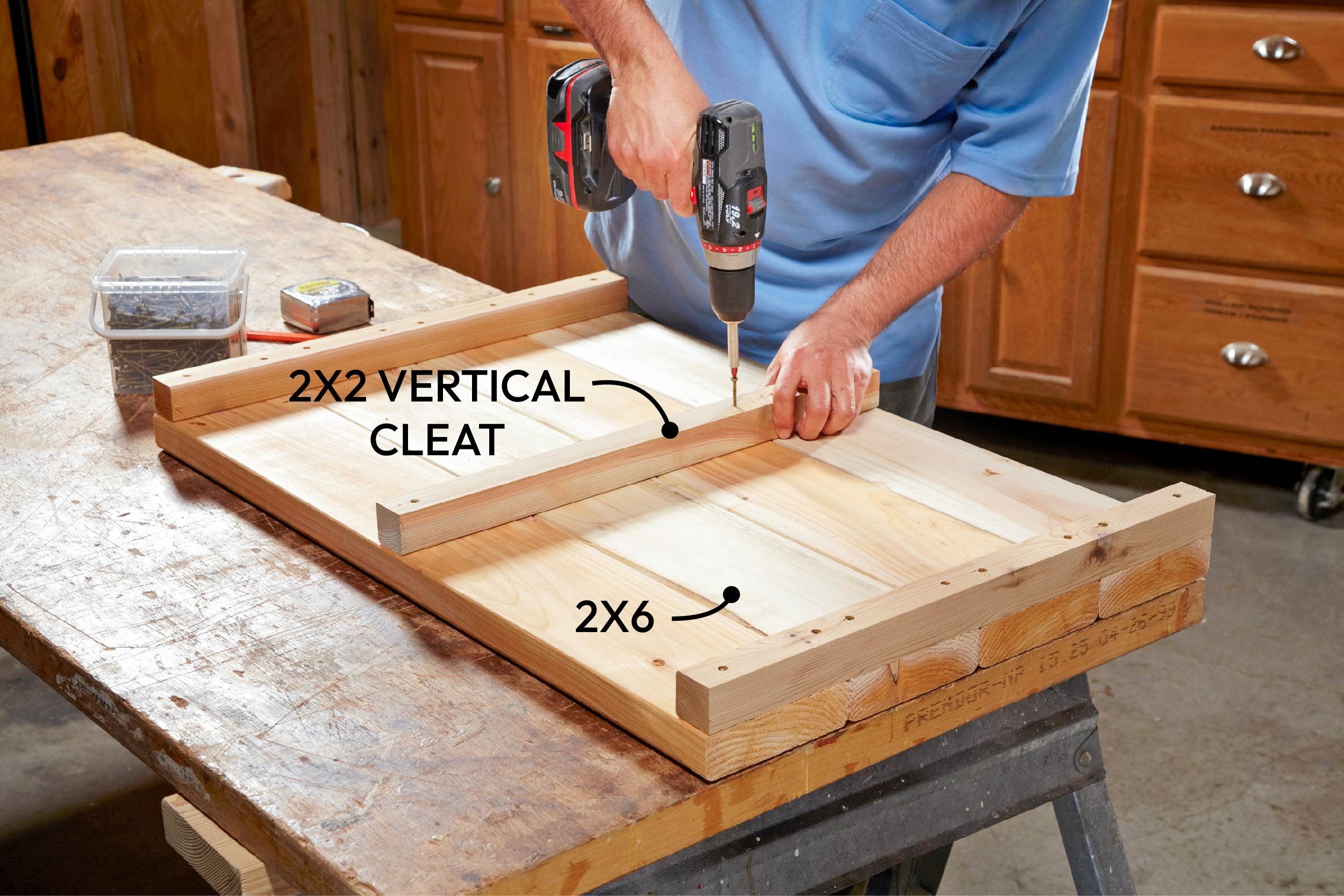 A person drills a screw into a wooden cleat, securing it onto a larger wooden panel on a workbench in a workshop environment.