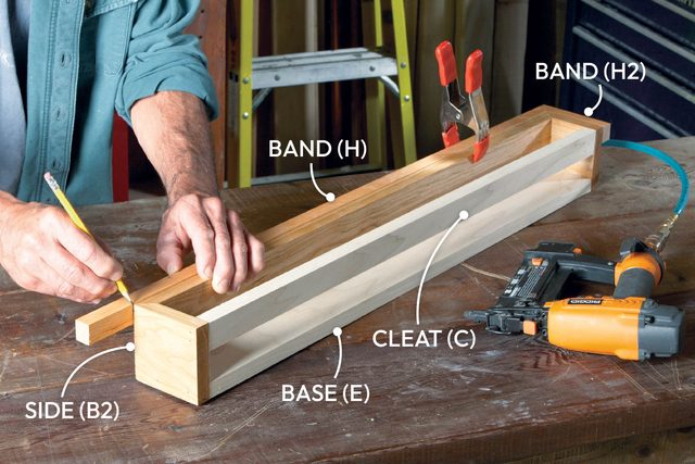 A person is measuring and marking wooden pieces on a workbench, surrounded by woodworking tools and materials in a well-lit workshop.