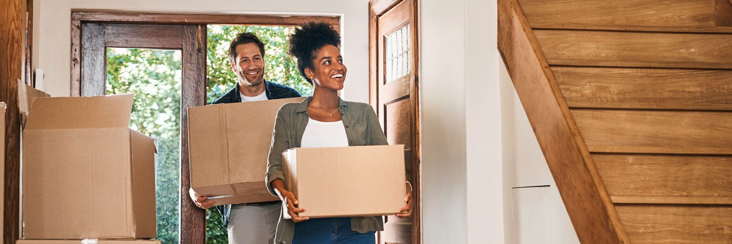 woman and man carrying boxes, moving in to their new home and looking around with happy, excited expressions