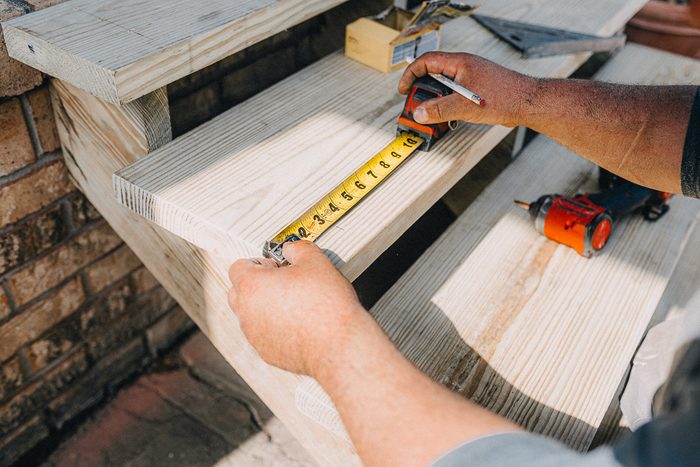 A person is using a tape measure to measure the width of a step while holding a pencil