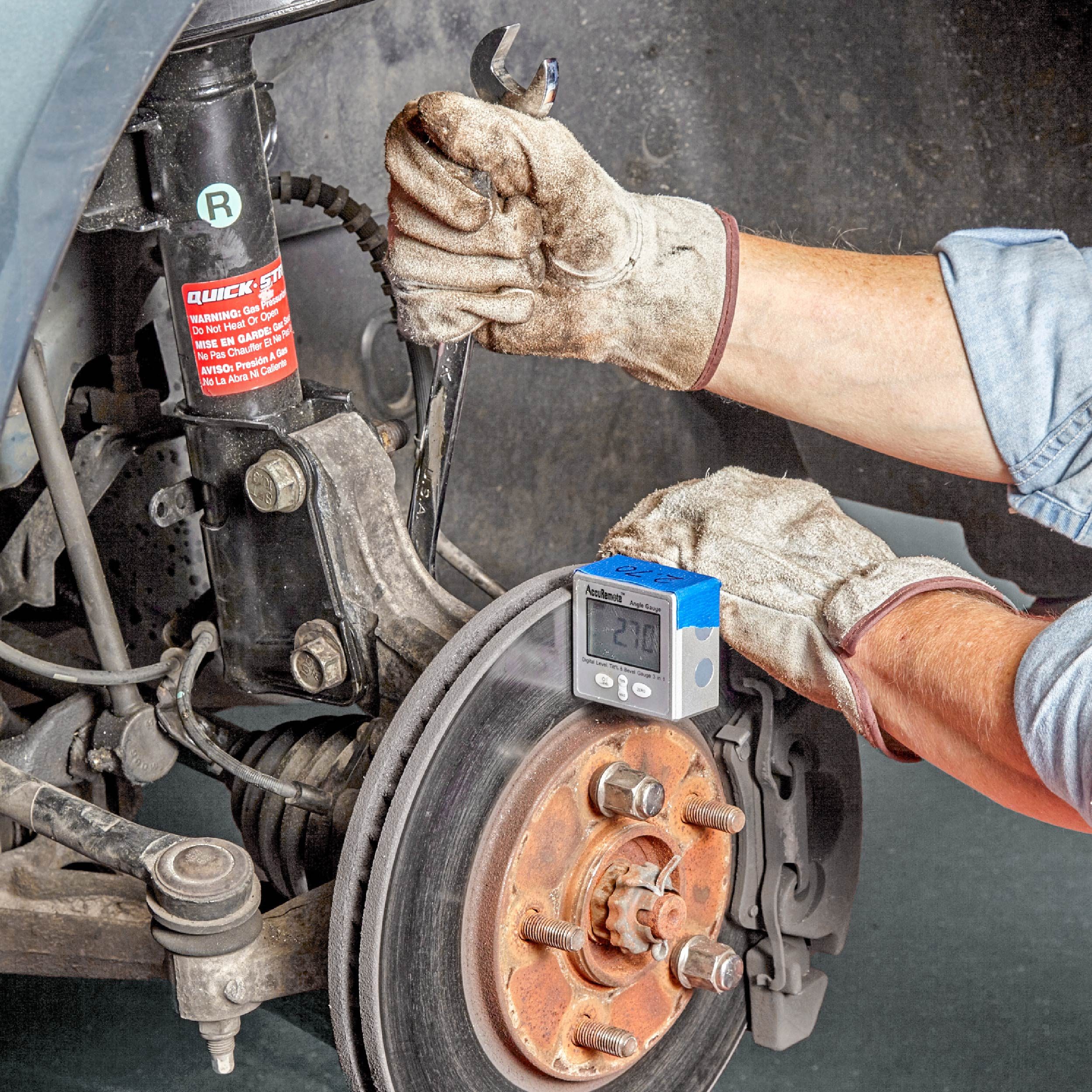 A hand holds a wrench, adjusting a car’s brake assembly, while a digital gauge displays a measurement, all inside a vehicle workshop.