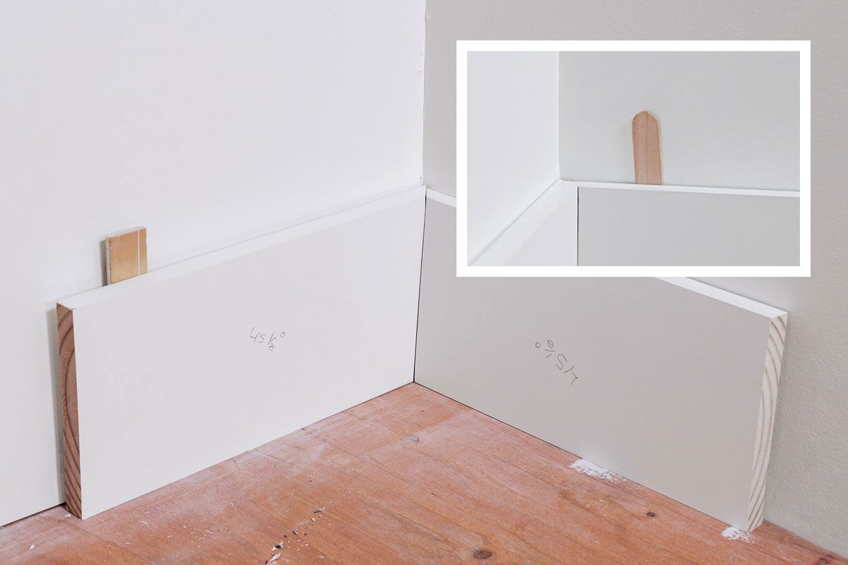 Closeup shot of a wooden popsicle stick wedged vertically in the corner where two white walls and a white surface meet;