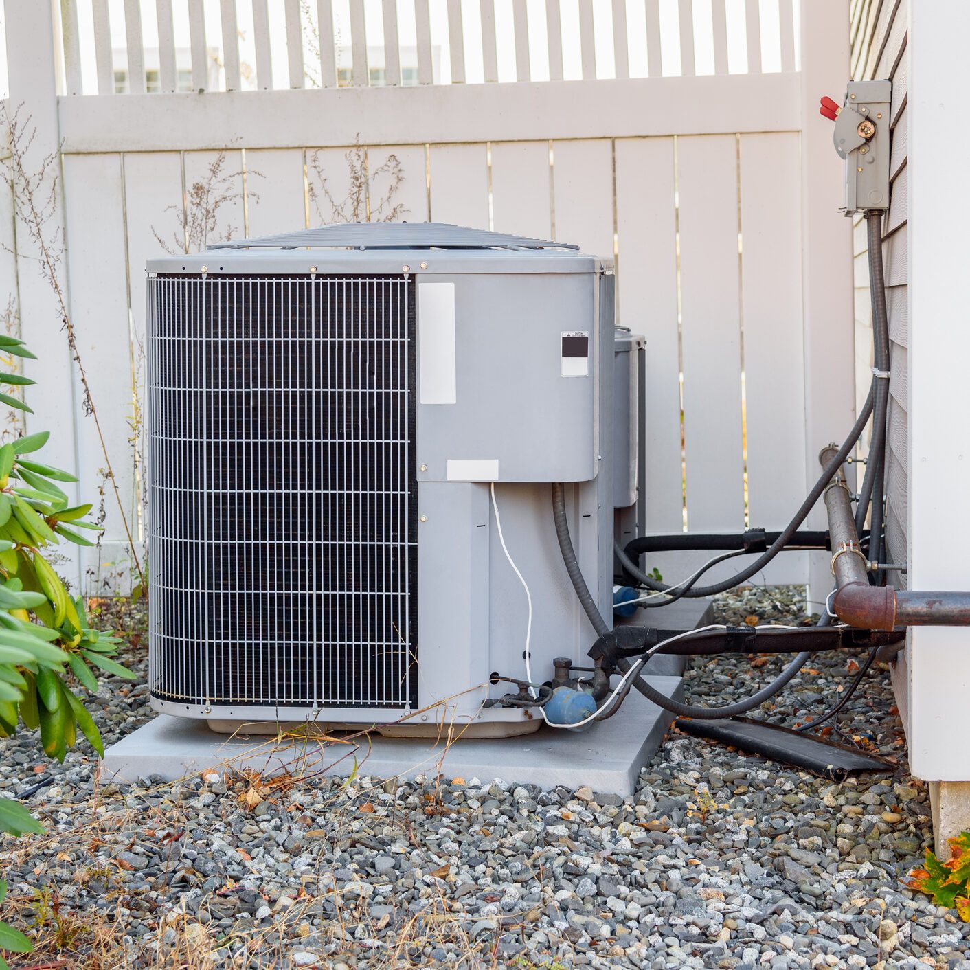 Air conditioning outdoor unit by a fence in a house backyard