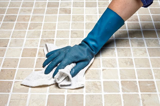 A person wearing a blue rubber glove is wiping a tiled surface with a white cloth.