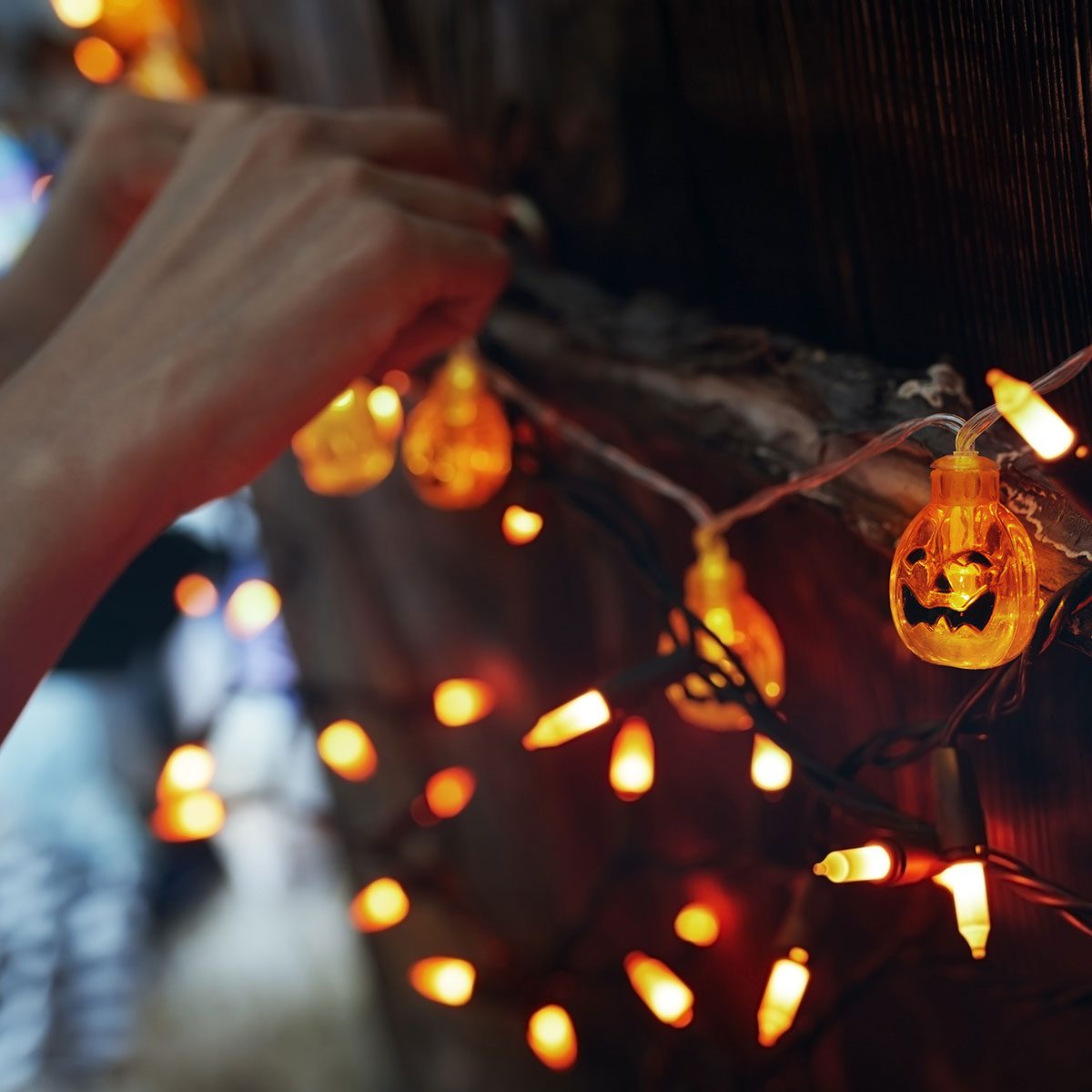 Woman hanging decorative eletric light with pumpkins. Halloween theme