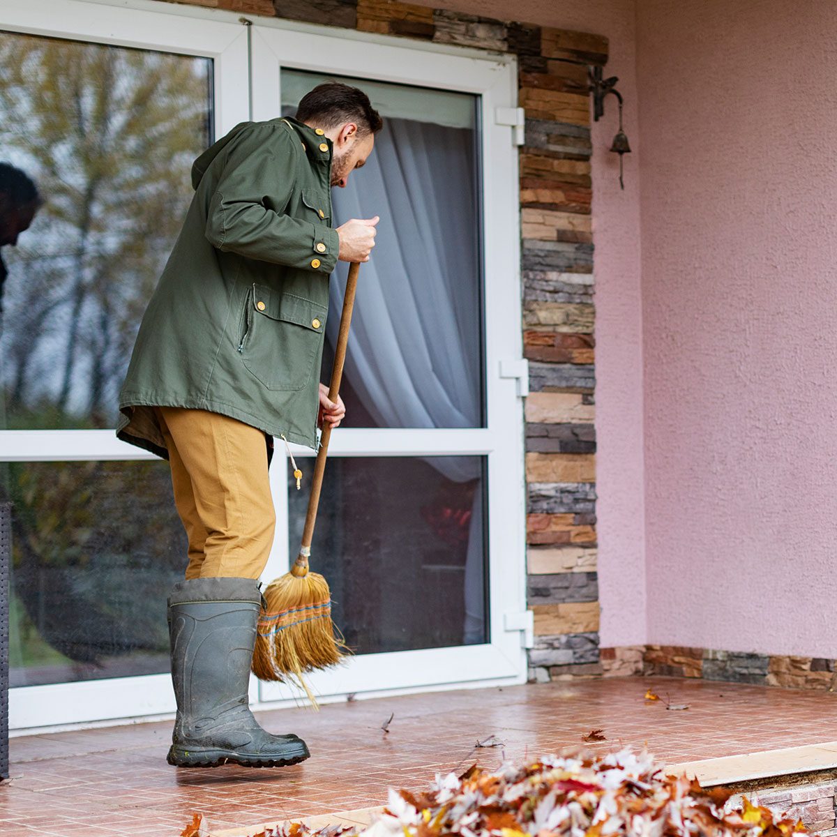 Adult man sweeping leaves from porch using broom