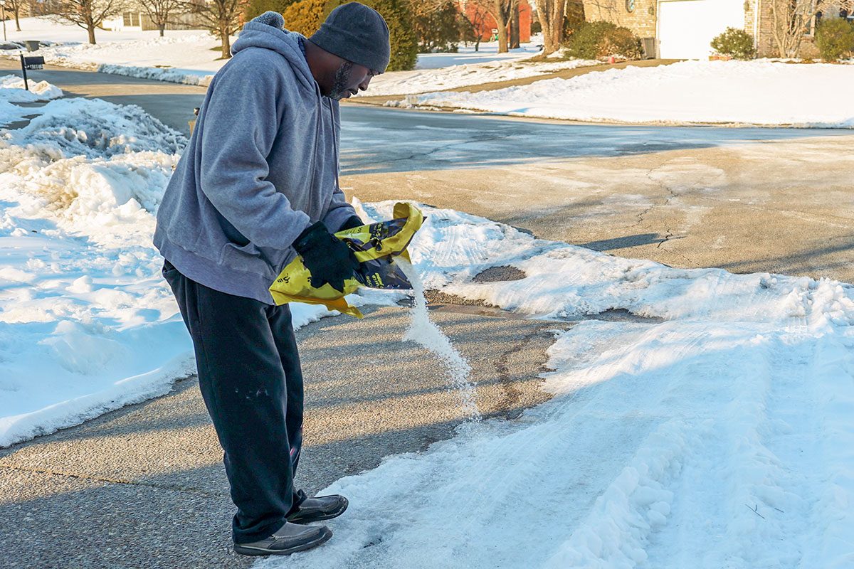 A portrait of a black man pouring a bag of salt on a icy driveway