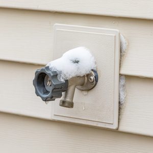 Outdoor water spigot covered in snow during winter. Home repair, maintenance and weatherproofing concept.