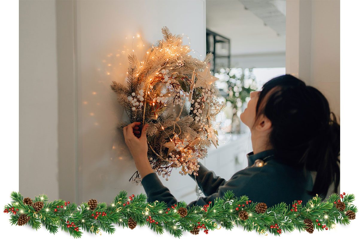 a young woman hanging a wreath to decorate the living room of her apartment; getting ready for the upcoming holiday season.