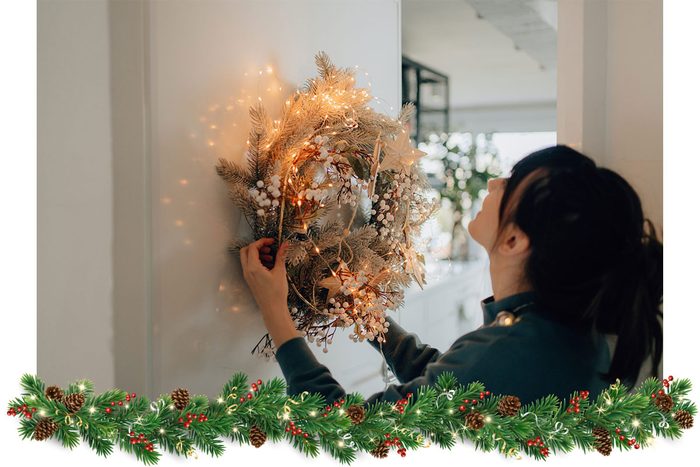 a young woman hanging a wreath to decorate the living room of her apartment; getting ready for the upcoming holiday season.