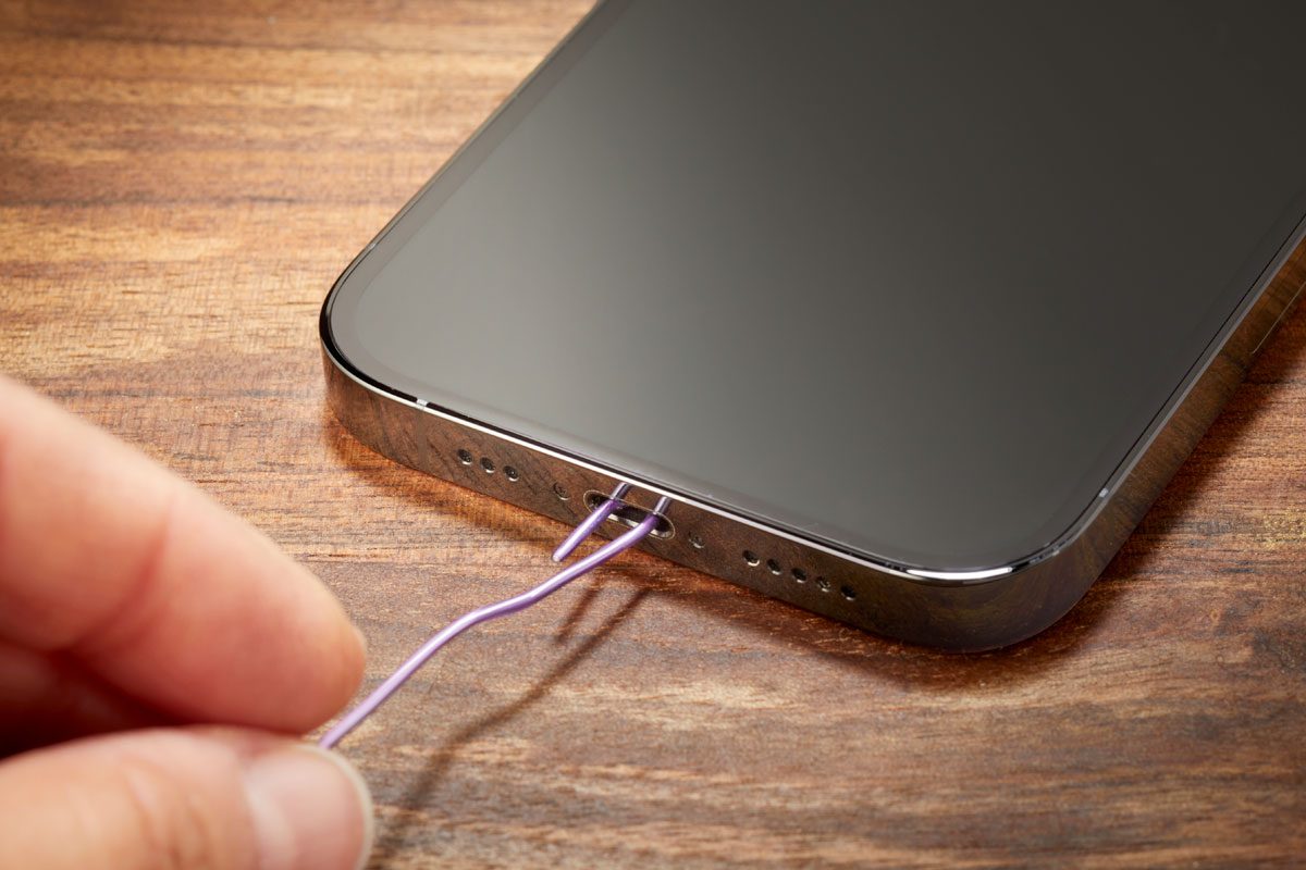 Hand using paper clip to clear dirt and debris from a smartphone charging port