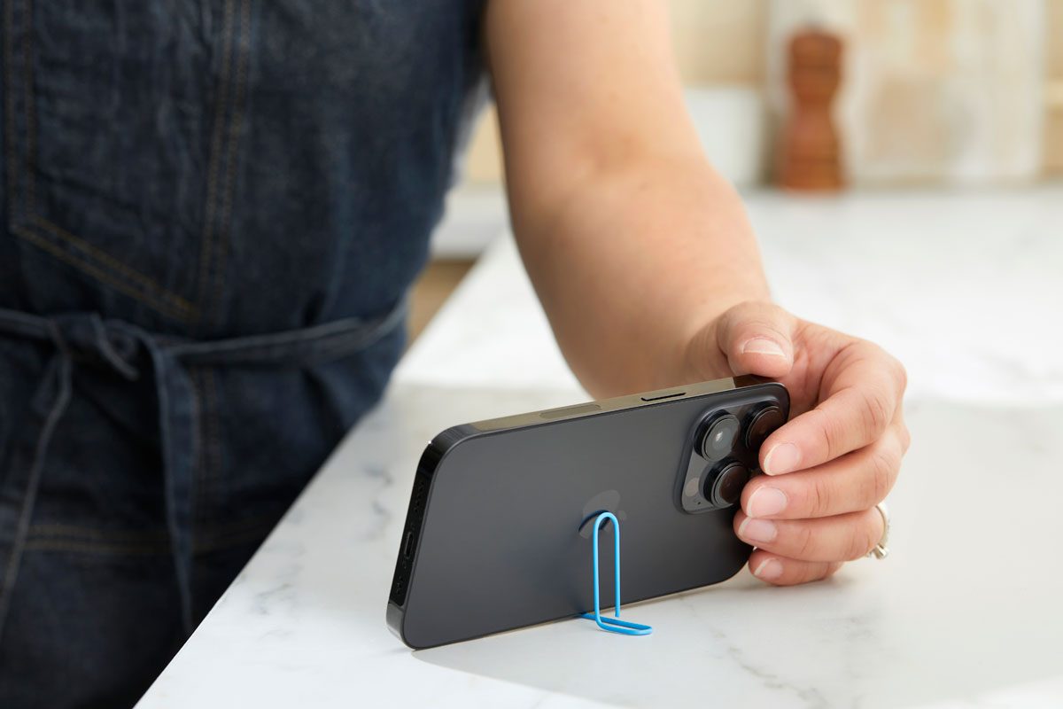 paper clip being used to prop up an iphone on a kitchen counter